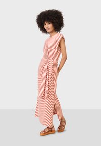 Gestreiftes Maxikleid aus roter und weißer Baumwolle mit gebundenem Taillenbereich, kurzen Ärmeln und seitlichen Schlitzen. Ergänzt durch braune Plattformsandalen.