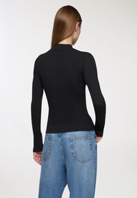 Czarny, długi rękaw, top o prążkowanej teksturze, dopasowany krój i wysoki dekolt, zestawiony z jasnoniebieskimi, postrzępionymi spodniami typu wide-leg.