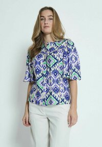 Blusa a maniche corte in un motivo geometrico viola e verde, realizzata in tessuto leggero, con chiusura a bottoni e vestibilità rilassata.