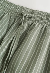 Hellegrüne gestreifte Hosen mit einem elastischen Bund und Kordelzug, gefertigt aus einem weichen Stoff mit glatter Textur.