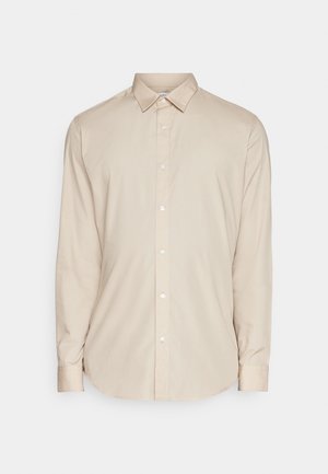 Chemise beige à manches longues, à col, dotée d'une coupe droite et d'une texture lisse. Elle possède des boutons blancs sur le devant.