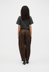 Μαύρο κοντό μπλουζάκι συνδυασμένο με καφέ παντελόνι καμπάνα με λεοπάρ τύπωμα. Λείο ύφασμα, ελαστική μέση και στενά μανσέτα, σε συνδυασμό με παπούτσια με χοντρό τακούνι.