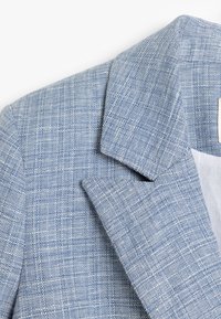 Lichtblauwe blazer van textuurstof, met scherpe revers en gestructureerde schouders, voorzien van een subtiel geruit patroon.