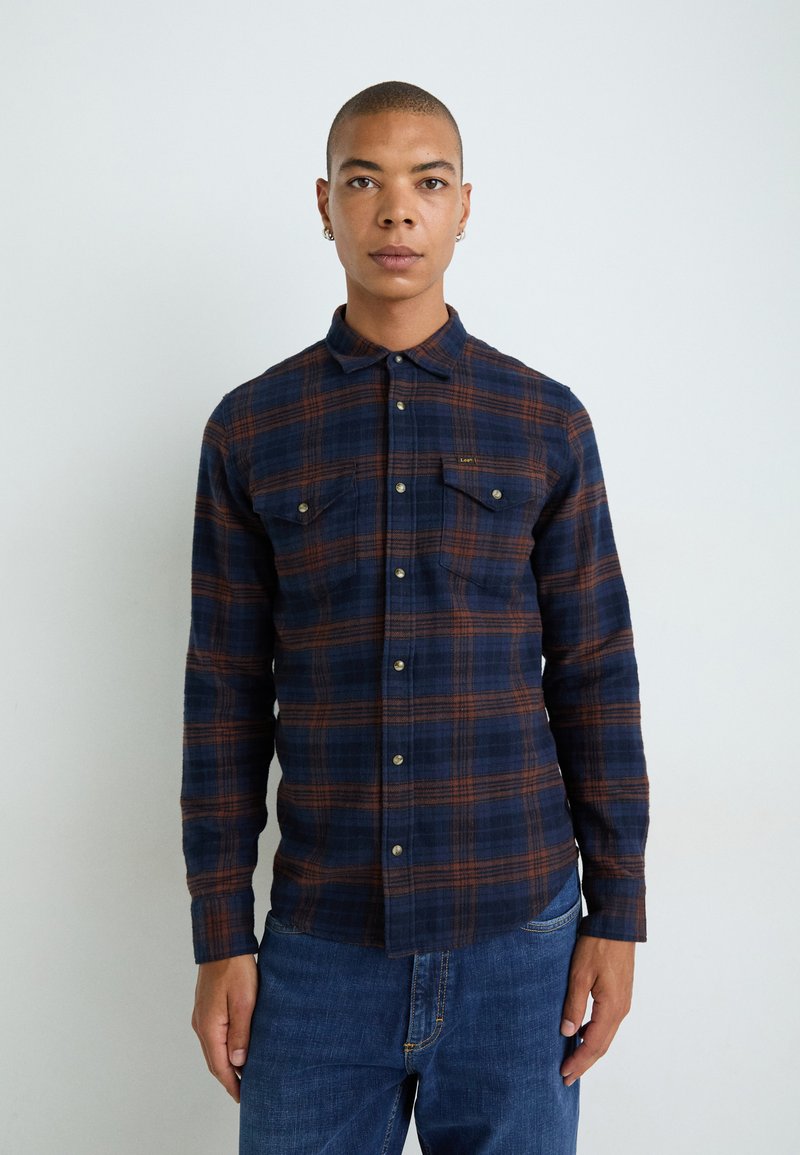 Marineblauwe geblokte shirt met oranje accenten, knoopsluiting aan de voorkant, twee borstzakken en lange mouwen in een zachte stof.