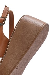 Sandale compensée en cuir marron avec bride ajustable et boucle, dotée de coutures blanches le long du bord de la semelle.