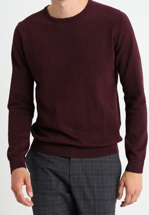Burgundy round-neck sweater in a smooth knit fabric, featuring long sleeves and a fitted waistband, paired with gray plaid trousers.