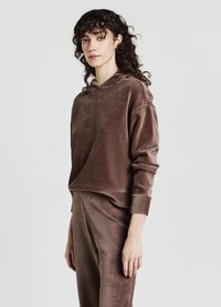 Felpa con cappuccio in velluto a coste marrone dal taglio comodo, con cappuccio e texture a coste. Abbinata a pantaloni coordinati, creando un completo coordinato.