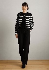 Černo-bílý pruhovaný cardigan s knoflíky, nošený přes černý top a široké černé kalhoty. Doplňkové příslušenství: černá kabelka.