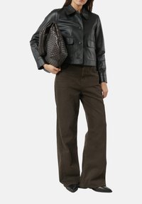 Schwarze Lederjacke in Cropped-Länge mit Kragen, zwei vorderen Taschen, kombiniert mit olivgrünen Hosen und einer strukturierten braunen gewebten Handtasche. Schwarze spitze Schuhe.