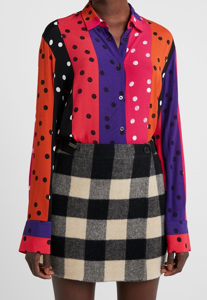 Chemise à manches longues aux couleurs vives avec des pois et des rayures ; associée à une jupe à carreaux noire et beige. Les deux sont en tissus lisses.