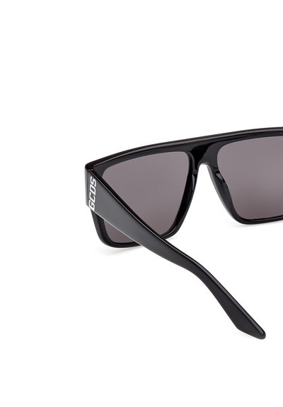 Czarne plastikowe okulary przeciwsłoneczne z ciemnoszarymi soczewkami; kanciasty kształt oprawki z logo po boku i smukłymi, zwężającymi się ramionami.