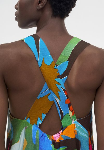 Άτομο που φοράει πολύχρωμο φόρεμα με λουλουδάτο μοτίβο και φαρδιές τιράντες που διασταυρώνονται στην ακάλυπτη πλάτη και τους ώμους.
