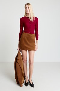 Haut boutonné à manches longues couleur bordeaux associé à une mini-jupe en daim marron, des escarpins noirs à bout pointu, et un blazer marron assorti.