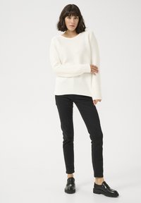 Maglione bianco a costine con maniche lunghe abbinato a pantaloni neri slim-fit e mocassini neri. Il maglione ha un collo rotondo e una vestibilità morbida.