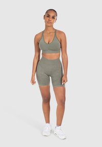 Conjunto deportivo de color verde oliva que incluye un sujetador deportivo con escote en V y fruncido, junto con unos pantalones cortos de talle alto a juego, fabricados con un material suave y elástico.