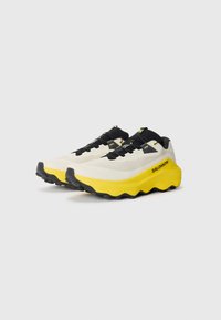 Baskets de course avec une tige en textile blanche, des accents noirs et une semelle jaune épaisse. Présente une surface texturée et une semelle extérieure en Vibram pour une meilleure adhérence.