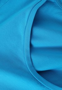 Helles blaues Baumwollgewebe mit glatter Textur; verfügt über einen runden Halsausschnitt mit einem kontrastierenden gerippten Saum. Keine sichtbaren Muster oder Akzente.