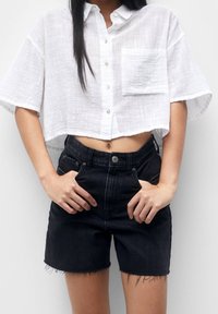 Chemise courte blanche texturée à manches courtes avec une poche, associée à un short en denim noir taille haute avec un ourlet effiloché.