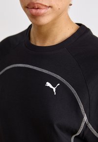 Mustmust-valgete õmblustega must sportlik särk, mille rinnal on Puma logo. Omab ümarat kaelaauku ja raglanvarrukaid, mis tagavad liikumisvabaduse.