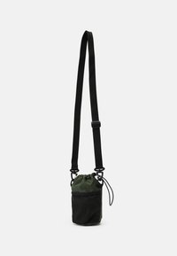 Saco sling de tecido verde com parte superior ajustada, painel de malha preta, alça ajustável e detalhes em metal para fecho seguro.