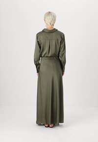 Robe longue vert olive avec un col, des manches à boutons et un dos plissé, présentant une texture de tissu fluide et lisse.