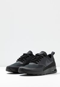 Une paire de baskets Nike Air Max noires avec des tiges en mesh et en synthétique, des semelles en caoutchouc épaisses et un amorti d'air visible sur une surface blanche.