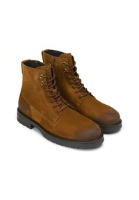 Paire de bottines à lacets en daim marron avec fermetures éclair latérales et semelles en caoutchouc noir sur fond blanc.