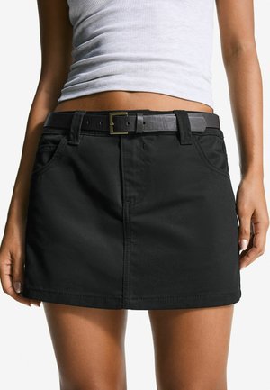 Black denim mini skirt with a fitted design, featuring a front pocket, belt loops, and a black leather belt with a gold buckle accent.