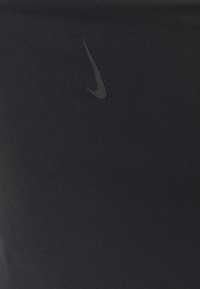Abbigliamento sportivo nero con un design elegante e una texture liscia, con un discreto logo Nike grigio nella parte inferiore.