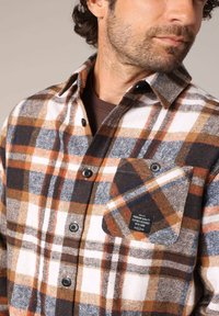Heren flanellen overhemd in een ruitpatroon met wit, oranje en donkerblauw. Voorzien van een knoopsluiting aan de voorkant en een linkerborstzak met label.