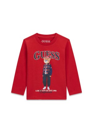 T-shirt rouge à manches longues avec un dessin d'ours debout en vêtements, logo "GUESS" au-dessus et texte "Los Angeles Est. 1981 California" en dessous.