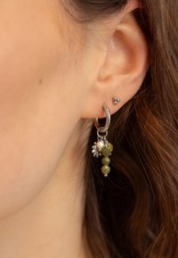 Orecchino a cerchio d'argento con perline di pietra verde e una perla, decorato con piccoli accenti floreali. Un altro piccolo orecchino a perno nell'orecchio.