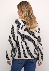 Pull ample en blanc avec des rayures zèbre noires. Fabriqué en tricot texturé, il présente des poignets et un ourlet côtelés. Coupe décontractée.