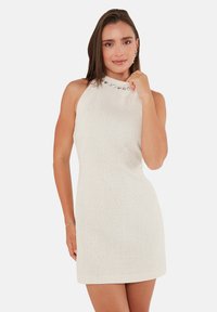 Robe sans manches blanche texturée avec un col montant et des accents de pierres décoratives le long du col, silhouette ajustée et longueur au-dessus du genou.
