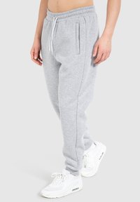 Joggers gris claro hechos de un suave forro polar, con cintura elástica, cordón y bolsillos laterales, combinados con zapatillas blancas.
