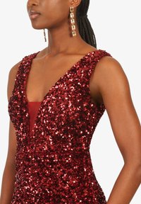 Rotes Pailletten-Kleid mit tiefem V-Ausschnitt und ärmellosem Design. Glatte Innenschicht, die durch dicht gepackte Pailletten schimmert.