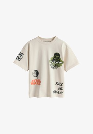 Bézs színű Star Wars póló Darth Vader grafikával, Halálcsillag illusztrációval, valamint "Star Wars", "Uralkodj a galaxisban" és "Sötét oldal" feliratokkal az ujjakon és az elején.