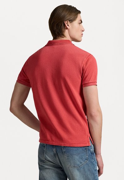 Rød polo skjorte med korte ermer, en klassisk krage, ribbede kanter og sideslisser, parret med blå denim jeans. Glatt bomullstekstur.