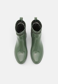 Botines verdes brillantes con un puño de punto verde texturizado, que cuentan con una puntera redondeada y un detalle de lengüeta en el talón.