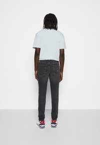 Camisa de manga corta azul claro con un corte relajado, combinada con jeans ajustados gris oscuro y zapatillas blancas con acentos rojos y azules.