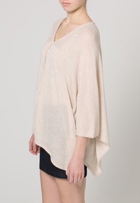 Tunica beige chiaro con tessuto a righe, scollatura a V e spacchi laterali, progettata con una vestibilità ampia e maniche a lunghezza gomito.