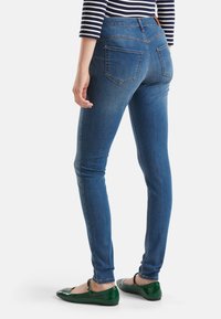 Smala jeans i mörkblå denim med en slät textur. Har hög midja, bakfickor och en sidsöm som framhäver benens form.