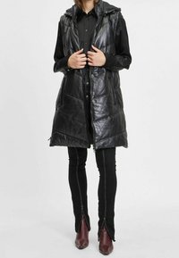 Czarna pikowana kamizelka z kapturem, o błyszczącej, pikowanej fakturze i przednim zamkiem błyskawicznym. Połączona z czarnymi obcisłymi jeansami i bordowymi botkami za kostkę.