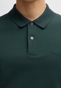 Grøn polo skjorte med tekstureret stof, to knapper ved kraven og broderet logo på venstre bryst. Standard pasform, korte ærmer.