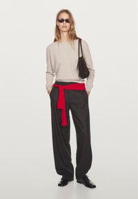 Beige stickad tröja, röd scarf knuten i midjan, grå byxor och svarta skor. Accessoar: brun axelväska och svarta solglasögon.