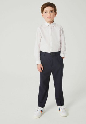 Camicia bianca a maniche lunghe con bottoni, pantaloni blu navy e sneakers bianche con strisce colorate. Tessuto di cotone liscio e vestibilità sagomata.