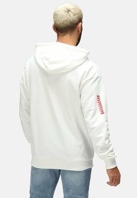 Weißer Hoodie mit Kordelzug, gerippten Bündchen und Saum. Auf dem linken Ärmel befindet sich der rote Schriftzug "BUCCANEERS". Der Stoff erscheint glatt und weich.
