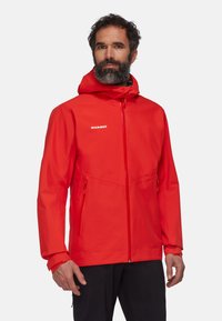 Giacca impermeabile rossa con cappuccio, dotata di tasche laterali con zip, polsini regolabili e un logo sul petto. Texture liscia.