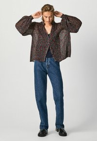 Blusa nera trasparente con motivo floreale, maniche a palloncino e chiusura a bottoni, abbinata a jeans in denim blu a vita alta.