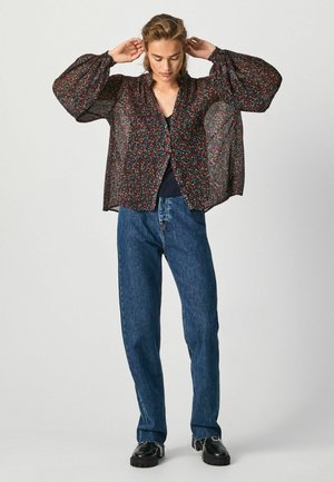 Blusa nera trasparente con motivo floreale, maniche a palloncino e chiusura a bottoni, abbinata a jeans in denim blu a vita alta.